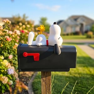May include: A black mailbox featuring a white Snoopy figure lying on top with a small yellow Woodstock figure perched on its back. The mailbox has a bright red flag attached to the side. The figures are smooth and matte in texture.
