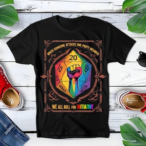 May include: Black t-shirt with a rainbow-colored 20-sided die with a fist in the center. The text "WHEN SOMEONE ATTACKS ONE PARTY MEMBER" is above the die and "WE ALL ROLL FOR INITIATIVE" is below the die.