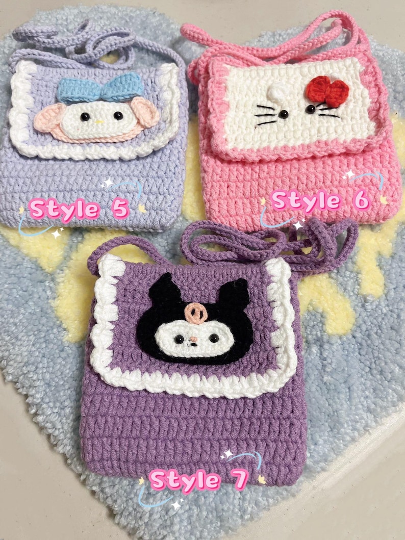 May include: Three crocheted purses with different character designs. The first purse is lavender with a white trim and a light blue and white character with a bow. The second purse is pink with a white trim and a white character with black eyes and a red bow. The third purse is purple with a white trim and a black character with white eyes and a pink nose. Each purse has a strap and the text "Style 5", "Style 6", and "Style 7" is written below each purse.