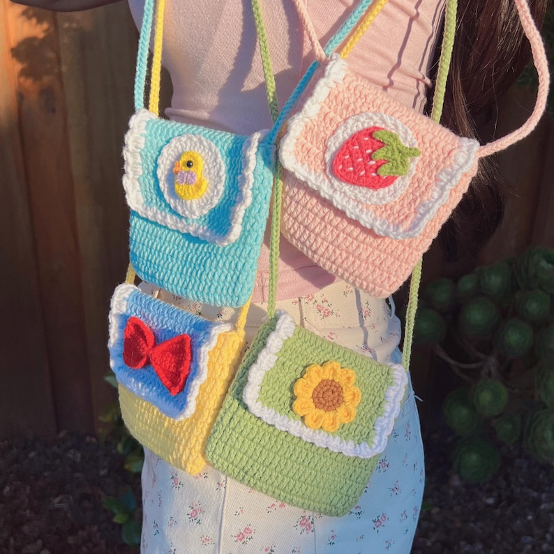 May include: Four small crocheted bags with different designs. The bags are light blue, pink, yellow, and green. Each bag has a different applique on the front: a duck, a strawberry, a bow, and a sunflower.
