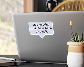 Pode incluir: Um autocolante em forma de balão de fala roxo claro com o texto preto, This meeting could have been an email. O autocolante está aplicado na parte de trás de um portátil prateado, colocado numa superfície escura junto a uma pequena planta.