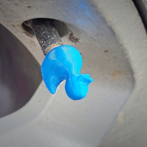 Puede incluir: Un tapón de válvula de neumático de goma azul con forma de pato.