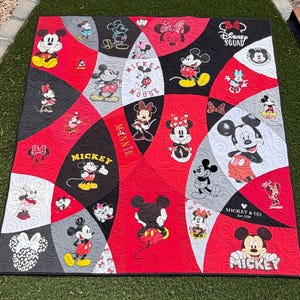 May include: A quilt featuring a patchwork design of red, black, white, and gray curved sections. The fabric displays various printed illustrations of Mickey Mouse and Minnie Mouse, along with text including Disney Squad, Mickey, Minnie, and Mickey & Co.