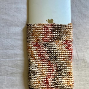 Può includere: Una custodia per laptop in maglia con un motivo a quadri colorati in tonalità di marrone, arancione, rosso e bianco.