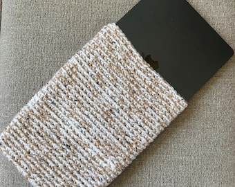 May include: A laptop computer partially inserted into a hand-knitted sleeve. The sleeve is made of a cream-colored yarn with brown and black flecks. The laptop is black.