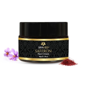 Puede incluir: Un tarro negro de crema facial Spaved Saffron con letras doradas sobre un fondo estampado en negro y dorado. El tarro está sobre una superficie blanca con una rama de flores de azafrán moradas y un montón de hebras de azafrán secas.