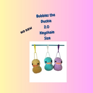 May include: Three plush duck keychains hanging from a metal bar. The ducks are yellow, teal, and purple. The text "Bubbles the Duckie 2.0 Keychain Size" is above the ducks. The text "NO SEW" is in the upper left corner of the image.