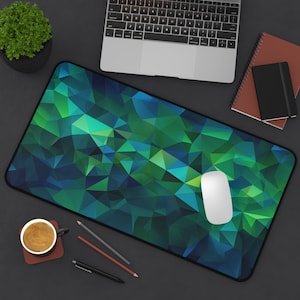 May include: A green and blue geometric patterned mousepad with a white computer mouse on top. The mousepad is on a dark gray surface with a laptop, a potted plant, and a brown notebook.