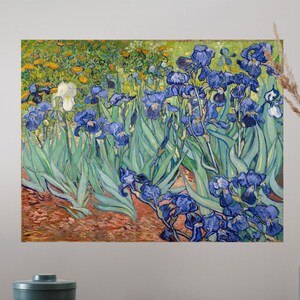 May include: A framed print of a painting featuring blue irises with green leaves and yellow flowers. The artwork is displayed above a wooden surface with a teal bowl, a gray cup, and a green vase with dried plants.