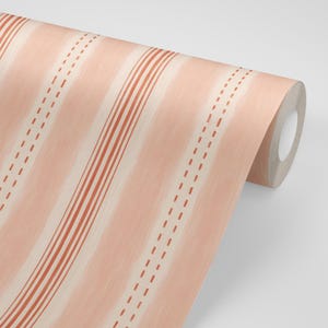 May include: A roll of wallpaper featuring a repeating pattern of vertical stripes in shades of light peach and terracotta. The design includes solid thick lines and parallel dashed lines, all set against a soft, textured, light peach background.