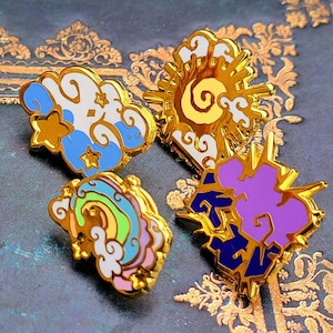 May include: Four enamel pins with gold accents. The pins feature a rainbow, a purple cloud with a lightning bolt, a blue and white cloud with stars, and a yellow sun with a swirl.