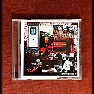 May include: A CD case with a collage of images, including a white door, a person in a yellow dress, and a panda bear. The text "Viewing Room" and "SAMPLE_TEXT" are visible. The case is on a red textured surface.