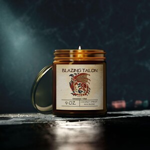 May include: A brown glass candle jar with a gold lid. The label reads "Blazing Talon" with a red and gold dragon illustration. The candle is 9 oz and has a scent of cinnamon and chai with a coconut apricot wax blend.