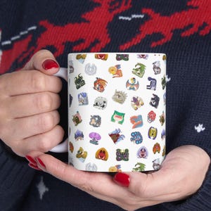Puede incluir: Taza de cerámica blanca con un patrón colorido de varios diseños de monstruos. La taza tiene un asa en el lado derecho.
