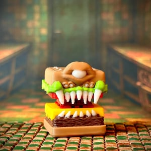 Puede incluir: Una cabeza de monstruo impresa en 3D con un esquema de color marrón, amarillo, rojo y verde. El monstruo tiene una boca grande con dientes afilados y un solo ojo.