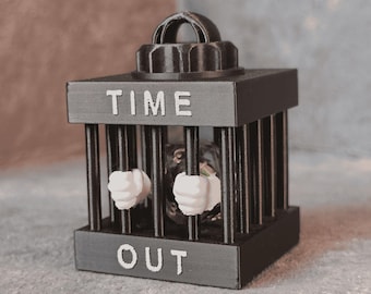 May include: A black, cage-like sculpture with the words "TIME OUT" in white lettering. Inside the cage are two white fists. The sculpture has a decorative top and is set against a neutral background.
