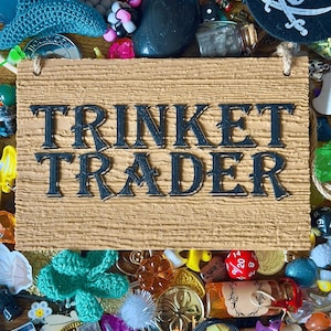 May include: A wooden sign reading "TRINKET TRADER" in dark blue lettering is surrounded by various trinkets. The trinkets include a pirate hat, dice, coins, and small figurines in a variety of colours.