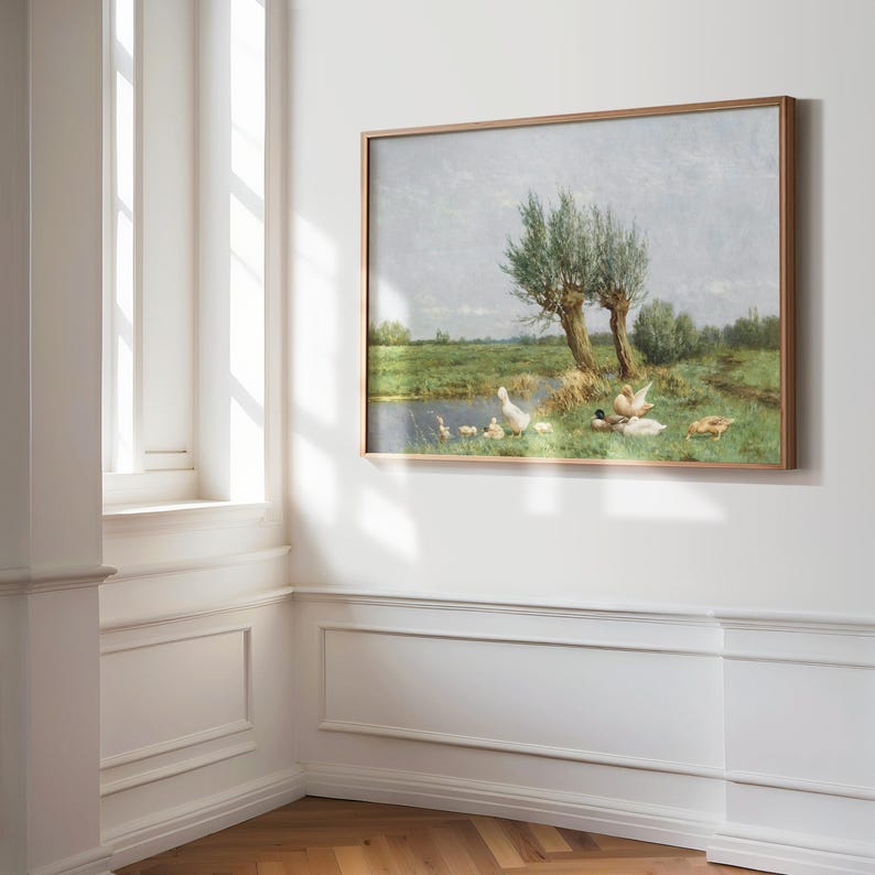 Op de afbeelding: Een ingelijst schilderij van een landelijk landschap met een vijver en een groep eenden. De eenden zijn wit, bruin en grijs en staan in het gras bij het water. Er zijn twee wilgenbomen op de achtergrond.