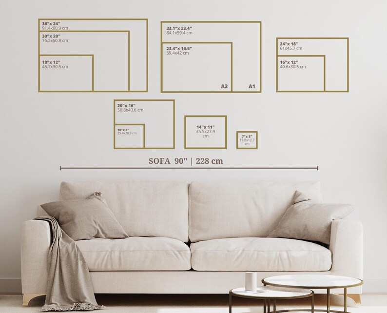 Op de afbeelding: Een witte bank met een bruin wollen deken erop. De bank is 90 inch (228 cm) lang. Aan de muur achter de bank hangen verschillende ingelijste foto's. De foto's zijn van verschillende grootte en zijn in een rasterpatroon gerangschikt. De foto's zijn allemaal in gouden lijsten. De tekst op de foto's geeft de grootte van de foto's in inches en centimeters aan.