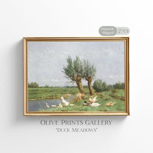 Op de afbeelding: Een ingelijst schilderij van een rustige weide sc&egrave;ne met een vijver en eenden. Het schilderij is getiteld "Duck Meadows" en is ingelijst in een gouden lijst.