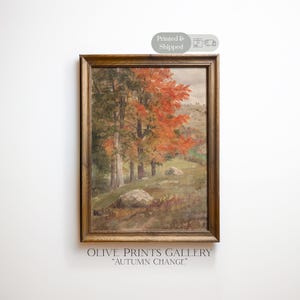 Puede incluir: Un cuadro de paisaje enmarcado titulado "Autumn Change" de Olive Prints Gallery, que muestra un grupo de árboles con follaje naranja y verde vibrante en una colina cubierta de hierba con rocas dispersas bajo un cielo nublado en un marco de madera.