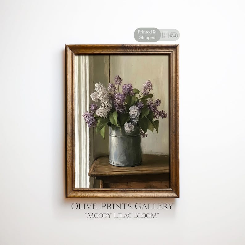 May include: A framed print of a still life featuring a bouquet of lilacs in a metal bucket. The flowers are a mix of purple and white, with green leaves. The print is labeled "Moody Lilac Bloom" by Olive Prints Gallery.
