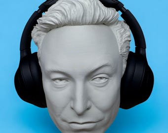 Puede incluir: Busto blanco de una persona con auriculares negros sobre un fondo azul. El busto tiene rasgos faciales detallados y cabello corto y texturizado. Los auriculares están colocados sobre las orejas y alrededor de la cabeza.