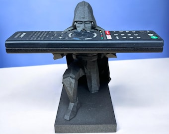 Puede incluir: Una figura de Darth Vader negra impresa en 3D que sostiene un mando a distancia negro en sus manos. La figura está arrodillada sobre una base negra.