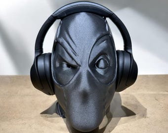 May include: A black 3D printed Deadpool head wearing black over-ear headphones. The headphones are on the head and the Deadpool head is looking straight ahead.