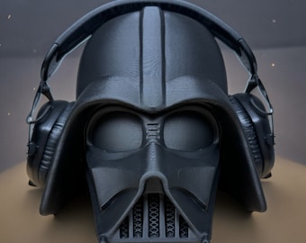 Puede incluir: Un casco negro de Darth Vader con auriculares. El casco tiene un diseño detallado y un acabado negro.