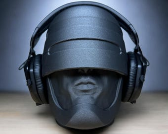 May include: A black, futuristic-looking helmet with headphones attached. The helmet has a visor that covers the eyes and a smooth, textured surface.