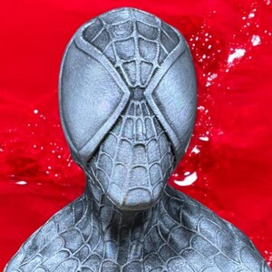 May include: A gray Spider-Man mask with a webbed design and large, oval eye openings. The mask is set against a vibrant red background, creating a striking contrast. The mask's texture and details are clearly visible.