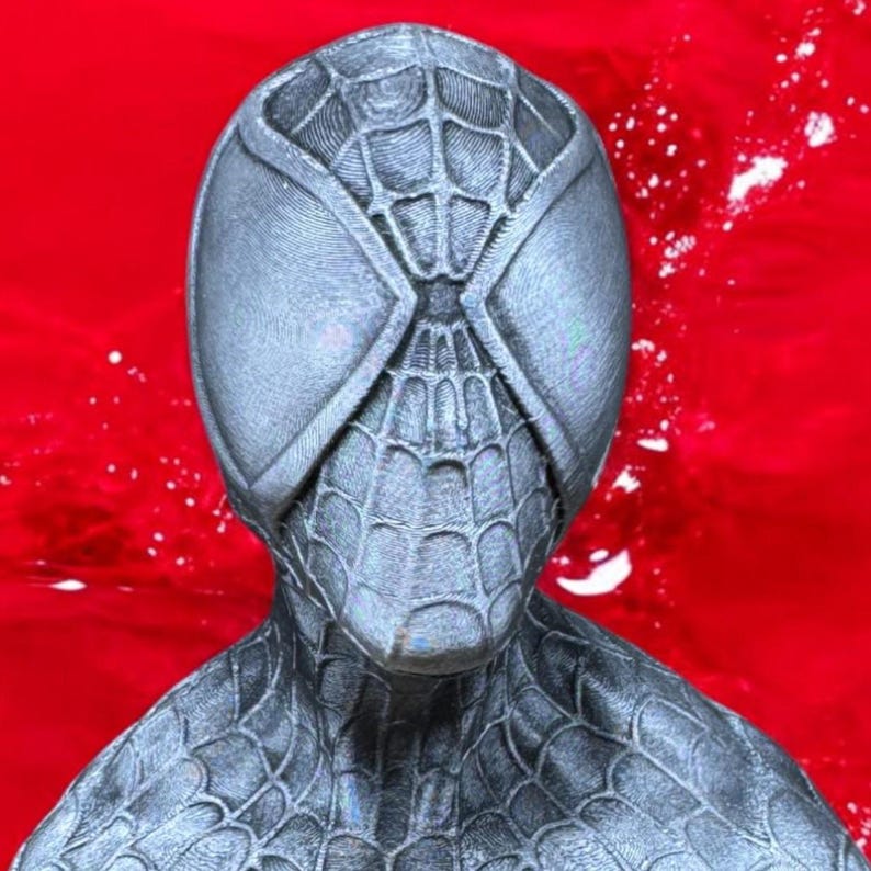 May include: A gray Spider-Man mask with a webbed design and large, oval eye openings. The mask is set against a vibrant red background, creating a striking contrast. The mask's texture and details are clearly visible.