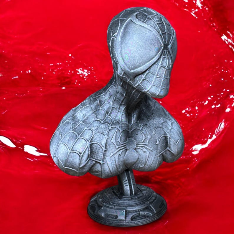 May include: A gray bust of Spider-Man, featuring the character's mask and torso. The bust is detailed with a spiderweb pattern and a spider emblem on the chest. It is set against a vibrant red background.