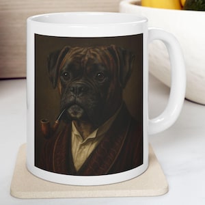 May include: White ceramic mug featuring a portrait of a Boxer dog wearing a robe and smoking a pipe. The dog is depicted in a vintage style with a brown and tan color palette. The mug has a white handle and a neutral-colored coaster.