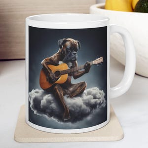 Puede incluir: Taza de cer&aacute;mica blanca con un perro Boxer tocando la guitarra ac&uacute;stica sentado en una nube. El perro es marr&oacute;n con hocico negro, y la guitarra es de color marr&oacute;n c&aacute;lido. El fondo es azul oscuro.