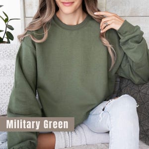 以下が含まれることがあります： 長袖のミリタリーグリーンのスウェットシャツ。「Military Green」の文字が画像の下部に表示されています。スウェットシャツは無地で、クルーネックです。
