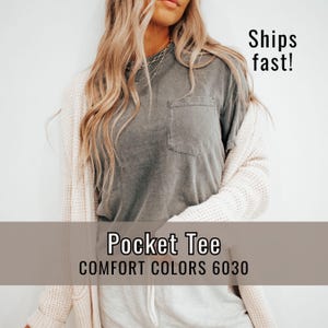 May include: A gray pocket tee shirt with the text "Pocket Tee" and "Comfort Colors 6030". The shirt is worn with a cream-colored cardigan. The text "Ships fast!" is also visible.