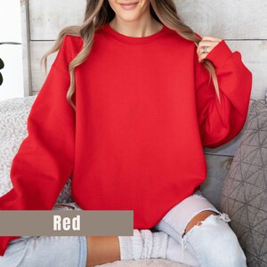 以下が含まれることがあります： 長袖の無地の赤いスウェットシャツ。画像の下部にある長方形のボックスに「Red」という単語が表示されています。スウェットシャツは柔らかい素材でできており、カジュアルなスタイルです。