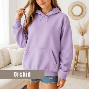 Op de afbeelding: Een lichtpaarse hoodie met een voorzak en een capuchon met trekkoord. Het woord "Orchid" wordt weergegeven in een rechthoekige doos onderaan de afbeelding. De hoodie is gemaakt van zacht materiaal en is geschikt voor vrijetijdskleding.