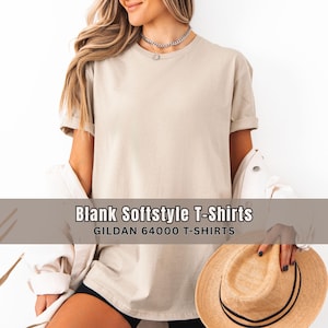 May include: A beige Gildan 64000 Softstyle T-shirt. The image shows a person wearing the shirt, with the sleeves rolled up. The text "Blank Softstyle T-Shirts" and "GILDAN 64000 T-SHIRTS" is displayed on a banner across the bottom of the image.