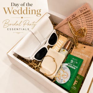May include: A gift box labeled Day of the Wedding Bridal Party Essentials containing white sunglasses, a gold metal hair claw, a wooden folding fan, a gold bangle, a tube of milk lip balm, a spray bottle, a cooling towel, and an aloe vera gel packet.