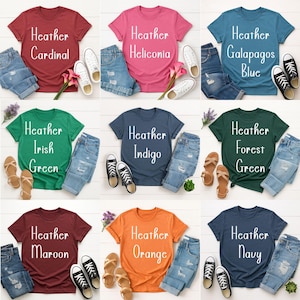 May include: A collection of colorful t-shirts with the words "Heather Cardinal", "Heather Heliconia", "Heather Galapagos Blue", "Heather Irish Green", "Heather Indigo", "Heather Forest Green", "Heather Maroon", "Heather Orange", and "Heather Navy" printed on them. Each shirt is paired with denim shorts and shoes.