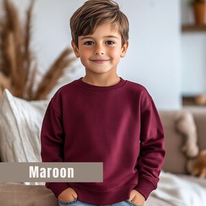 May include: A maroon crewneck sweatshirt. The sweatshirt is a solid color and has a classic, simple design. The word "Maroon" is displayed in a rectangular box at the bottom of the image. The sweatshirt is likely made of a soft, comfortable material.
