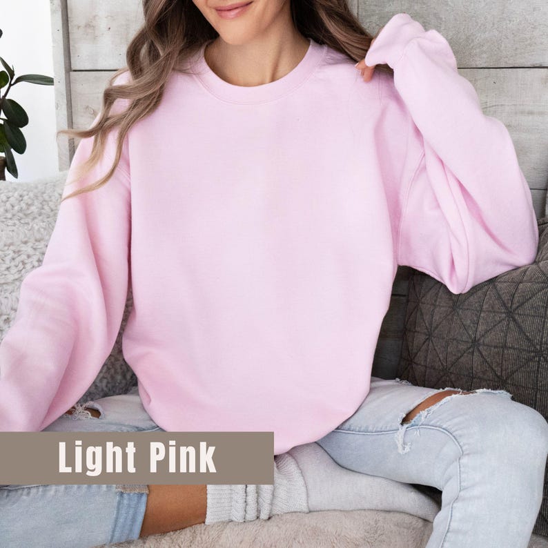 以下が含まれることがあります： 長袖のライトピンクのスウェットシャツ。「Light Pink」の文字が画像の下部にある長方形のボックスに表示されています。スウェットシャツは無地で、柔らかい素材でできているようです。