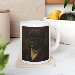 Puede incluir: Taza de cer&aacute;mica blanca con un retrato de un perro Boxer con un esmoquin y fumando en pipa. El perro est&aacute; representado en un estilo vintage con una paleta de colores marr&oacute;n y beige. La taza tiene un asa curva.
