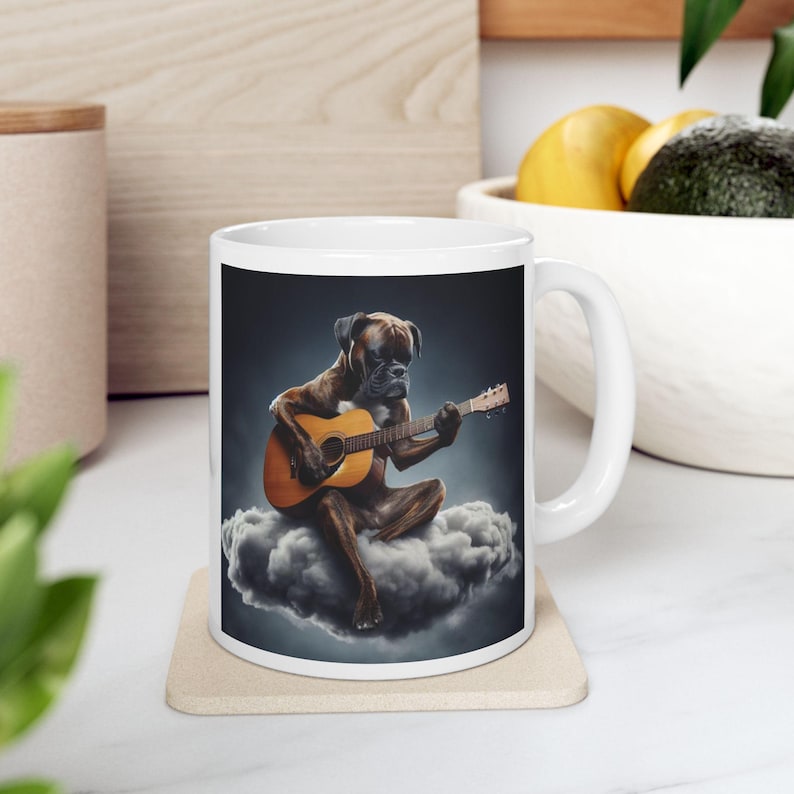 Puede incluir: Taza de cer&aacute;mica blanca con un perro Boxer tocando la guitarra ac&uacute;stica sentado en una nube. El perro es marr&oacute;n con hocico negro, y la guitarra es de color marr&oacute;n c&aacute;lido. El fondo es azul oscuro.