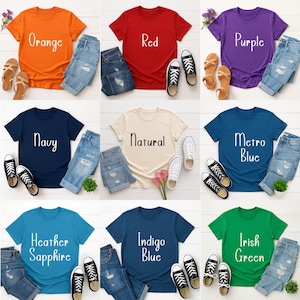 May include: A collection of t-shirts in various colors, including orange, red, purple, navy, natural, metro blue, heather sapphire, indigo blue, and Irish green. Each shirt is paired with denim shorts, sandals, and sneakers. The shirts have text on them.