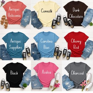 May include: A collection of t-shirts in various colors, including red, yellow, blue, and black, each paired with denim shorts and sneakers. The shirts display text such as "Antique Heliconia," "Cornsilk," and "Carolina Blue."