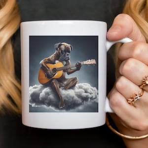May include: A white ceramic mug with a brown and white boxer dog playing a brown acoustic guitar on a white cloud. The dog is sitting on the cloud and has a serious expression on its face.